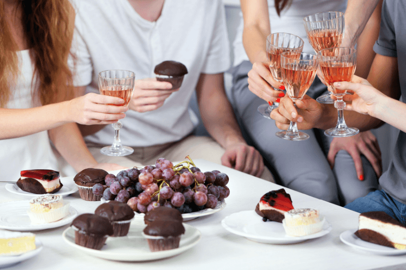 Friends toasting dessert wine with cakes, cupcakes, and fresh grapes on table