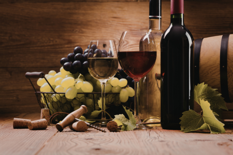 Red and white wine glasses with bottles, corks, and fresh grapes on rustic wooden table