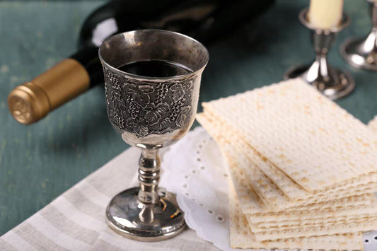 Silver Kiddush cup filled with kosher wine beside matzo and a wine bottle