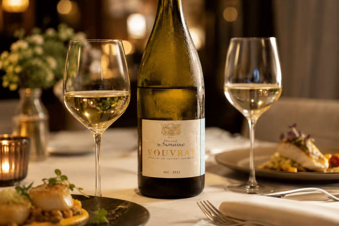 Vouvray wine bottle with two glasses of white wine and plated food at an elegant dinner table