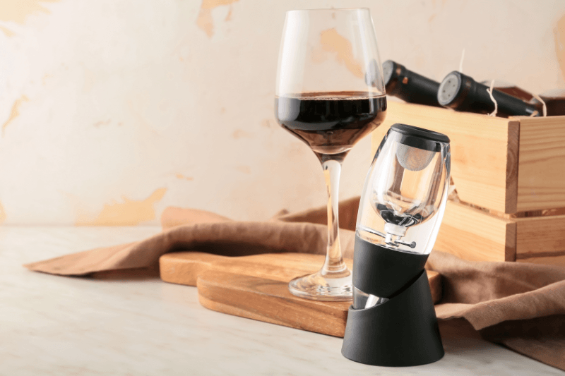 Wine aerator device next to a glass of red wine and wine bottles