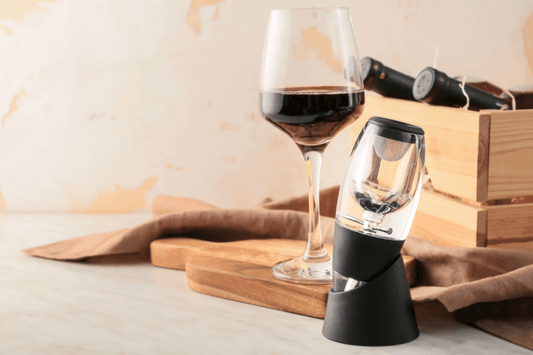 Wine aerator device next to a glass of red wine and wine bottles